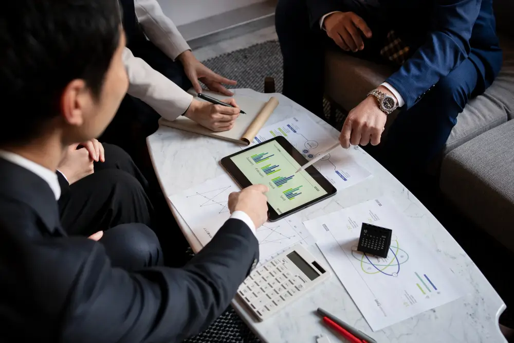 Business people pointing at a tablet with financial charts during a meeting, with documents and calculator on the table